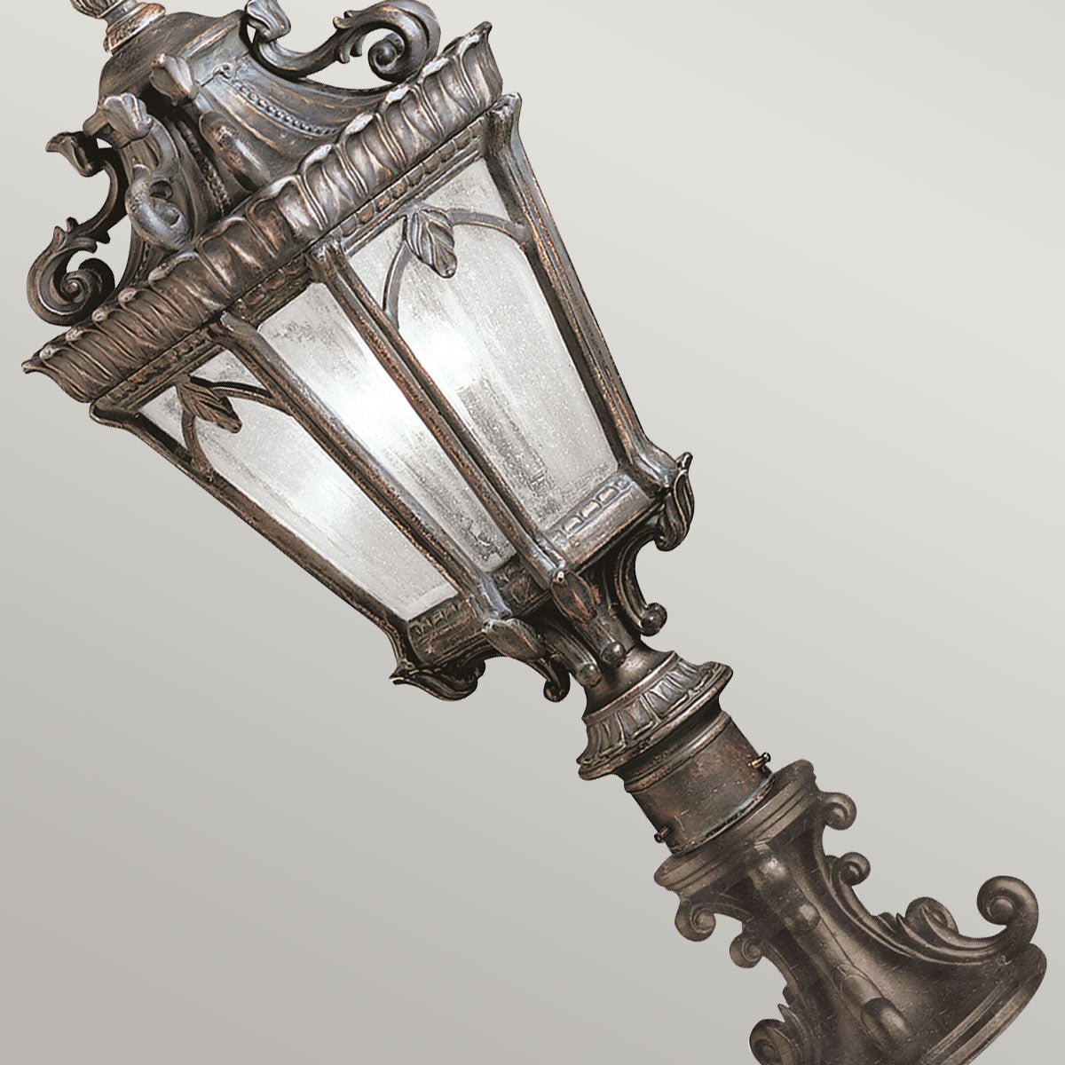 Vue en plongée du lampadaire, lanterne et base sculptée sur fond gris.