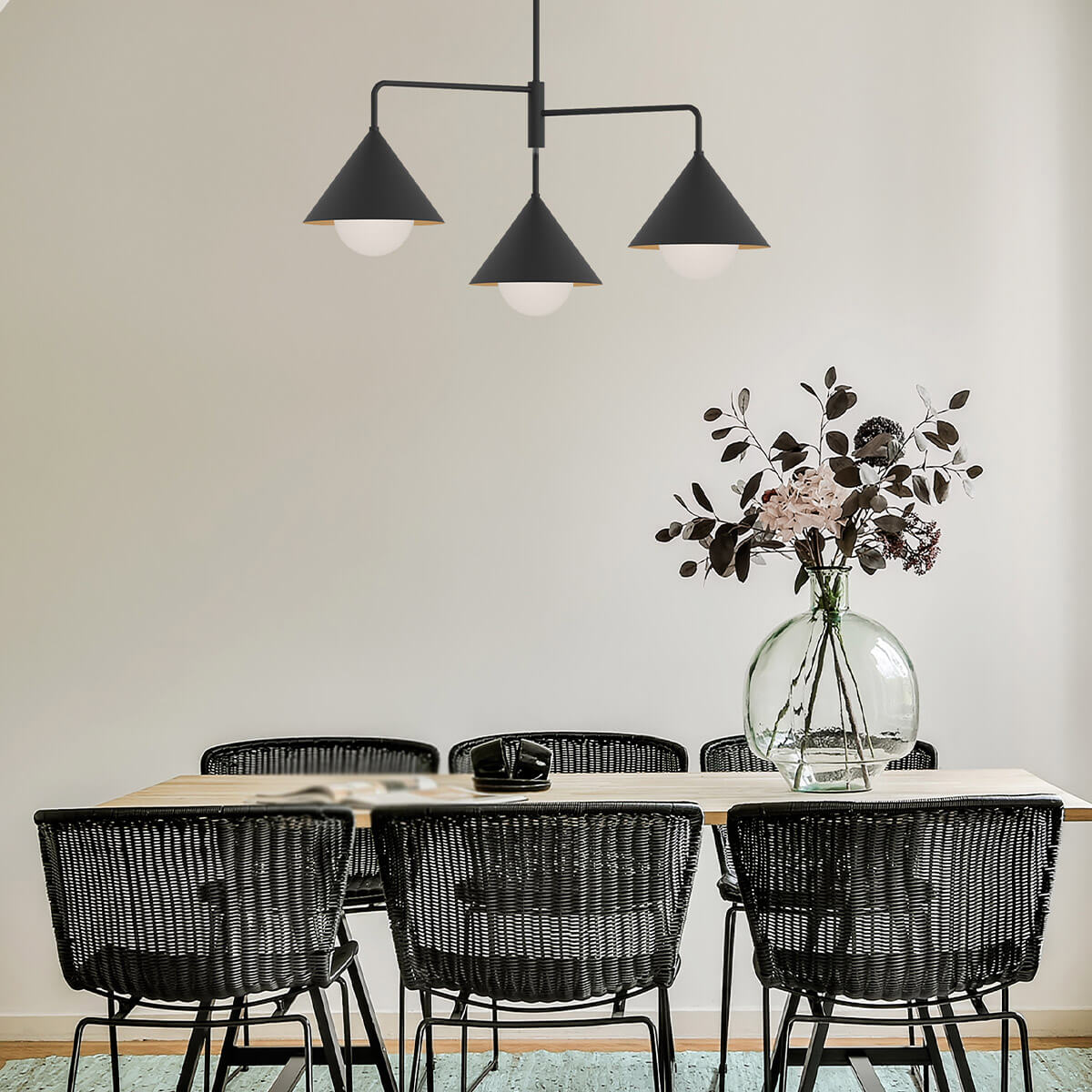 Mise en ambiance au-dessus d'une table à manger avec chaises noires et vase transparent.