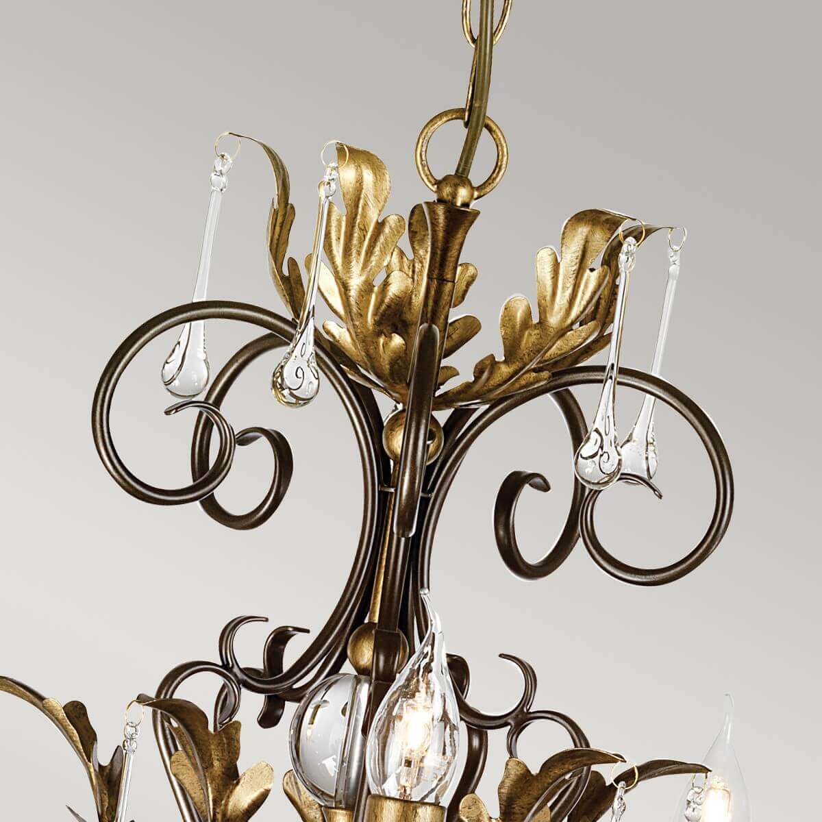 Détail du sommet : feuilles dorées, boucles bronze et gouttes de verre transparent.