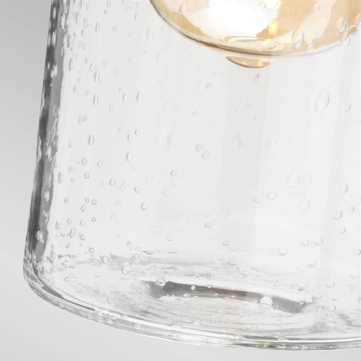 Détail du verre moucheté transparent laissant voir l'ampoule dorée illuminée