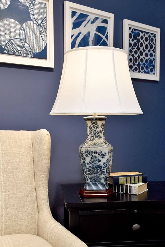 Lampe posée sur une table de nuit noire dans un salon bleu avec fauteuil.