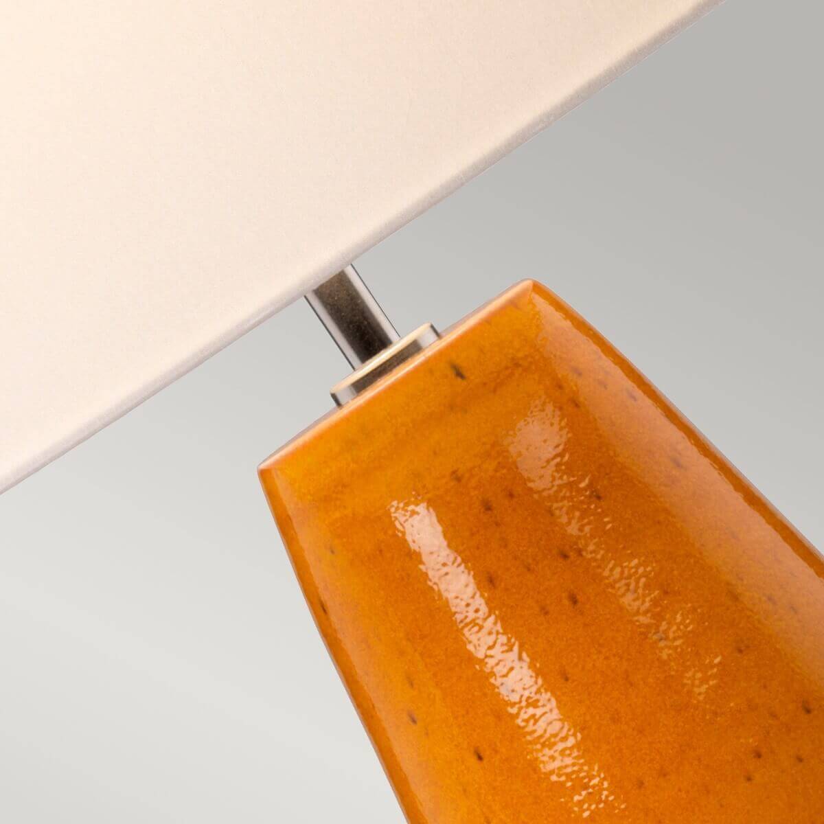Détail du raccord métallique entre l'abat-jour ivoire et le haut du pied en céramique orangée tachetée.