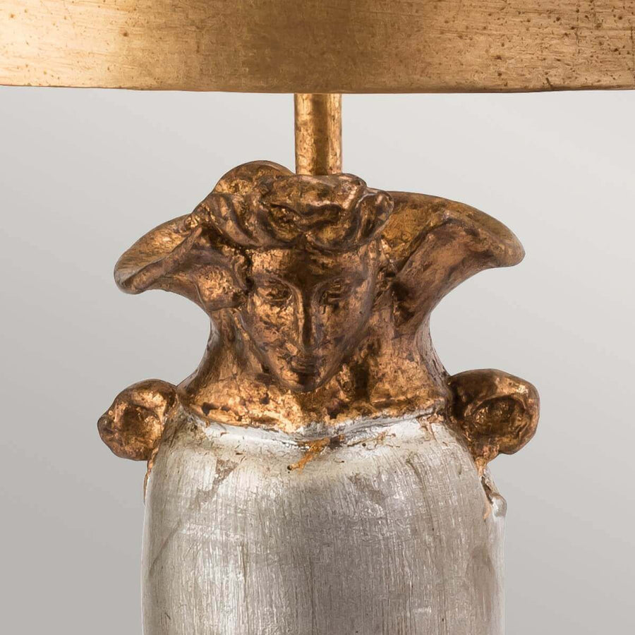 Détail du sommet de la base sculpté d'un visage doré et d'anses.