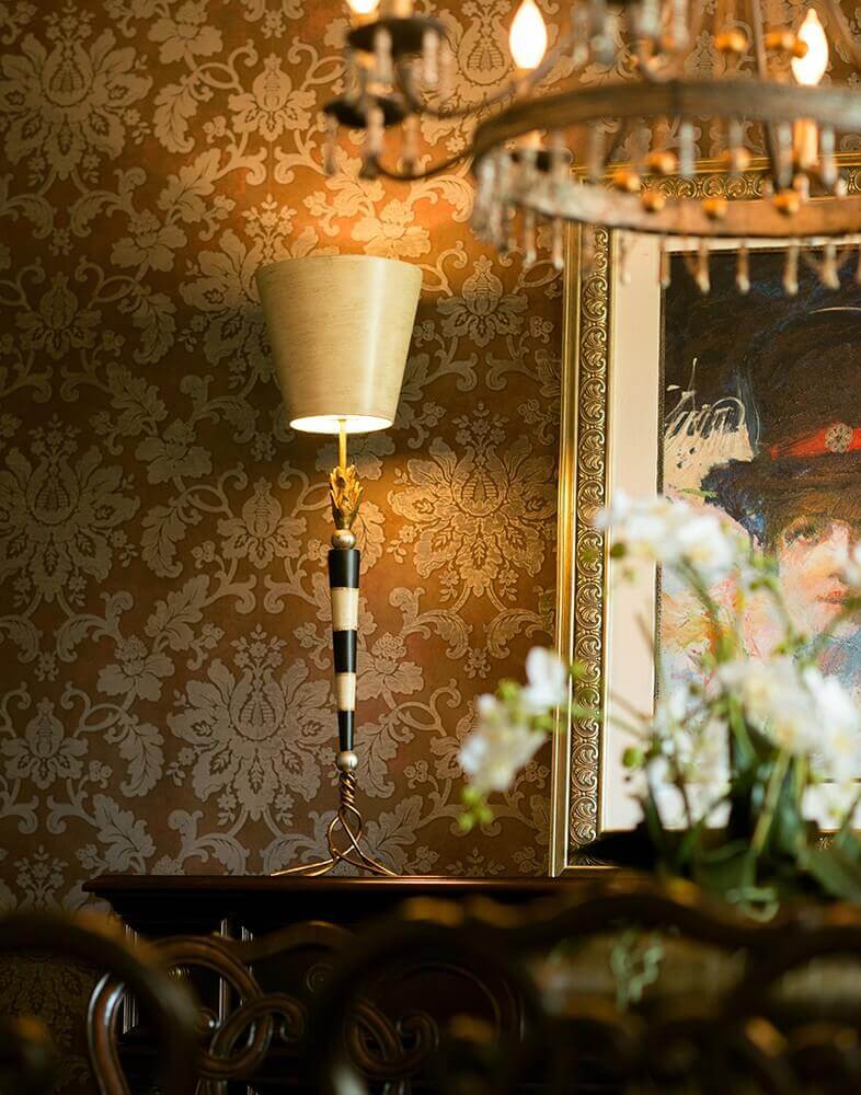 Lampe posée sur console, abat-jour crème et fût rayé, papier peint fleuri et tableau.