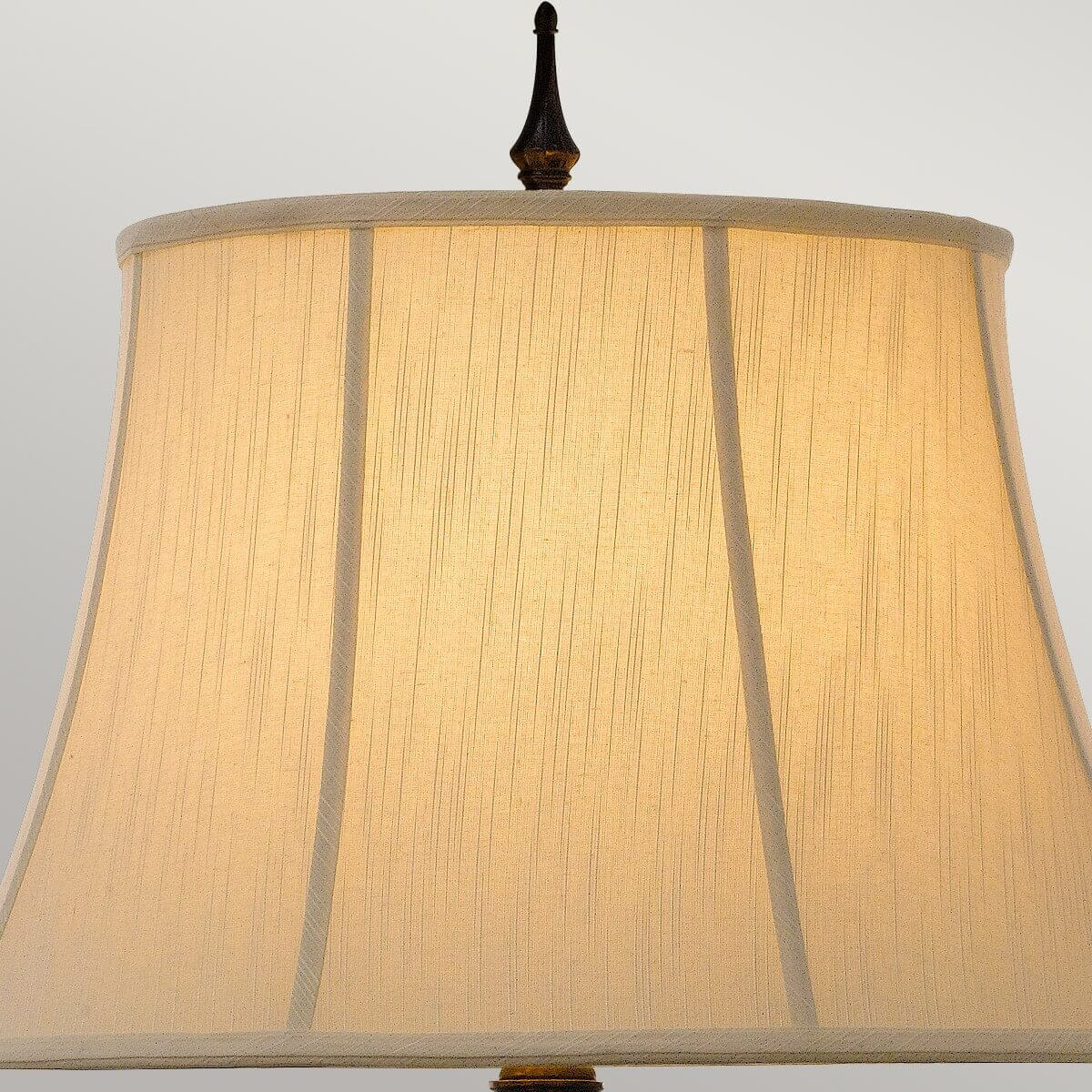 Gros plan sur l'abat-jour textile beige et sa finition sommitale en métal foncé.