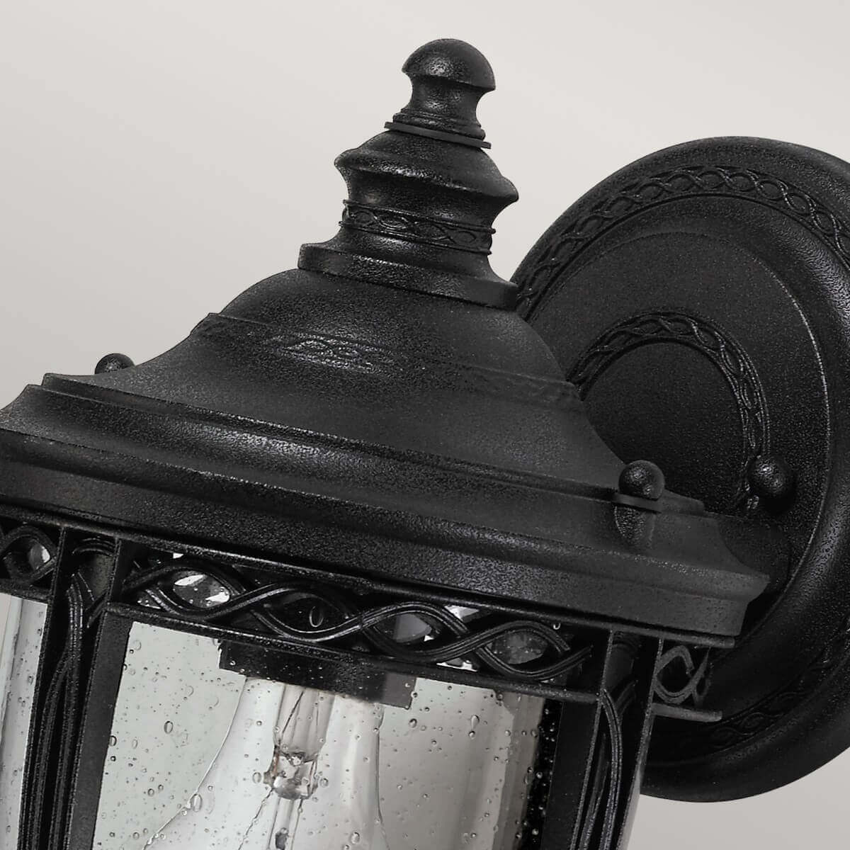 Détail du chapeau sommital noir et de la platine murale ronde ornée.