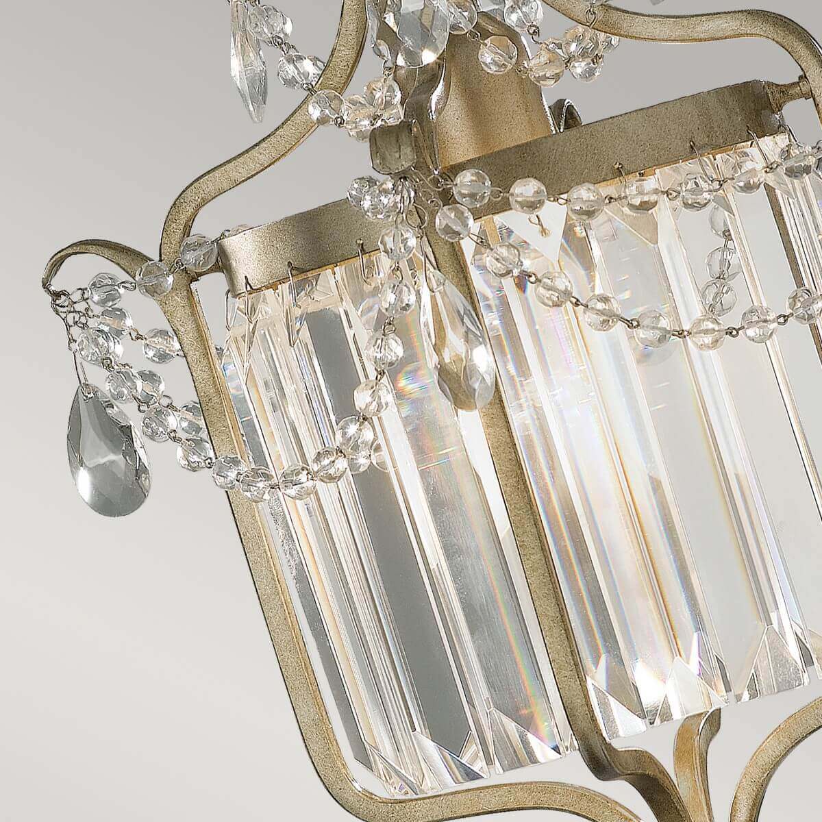 Gros plan sur les prismes de cristal, chaînette perlée et reflets irisés sur la structure métallique.
