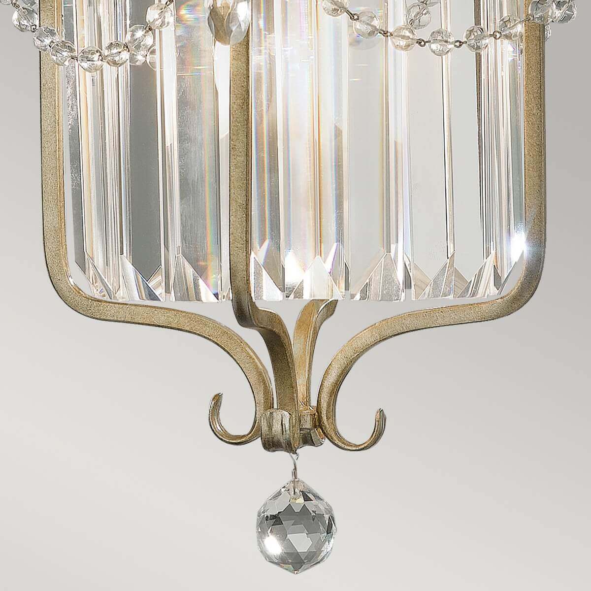 Détail du bas : boule de cristal facettée suspendue sous les volutes métalliques dorées et argentées.