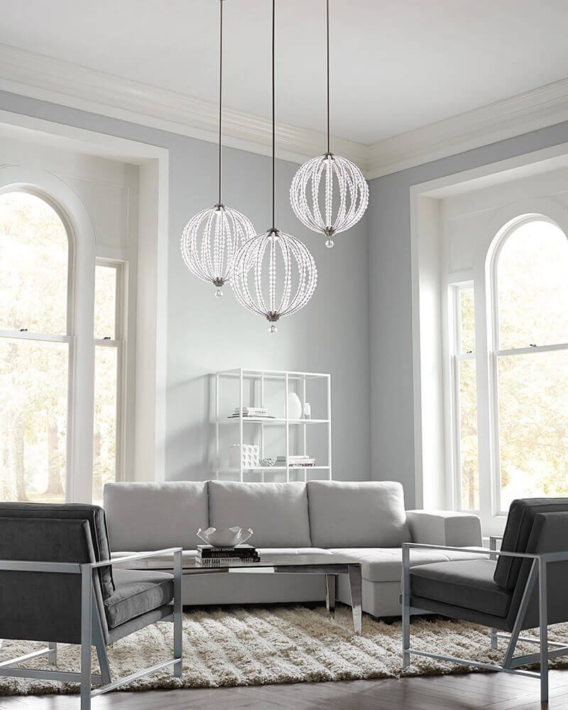 Trois suspensions allumées au-dessus d'un salon gris et blanc.
