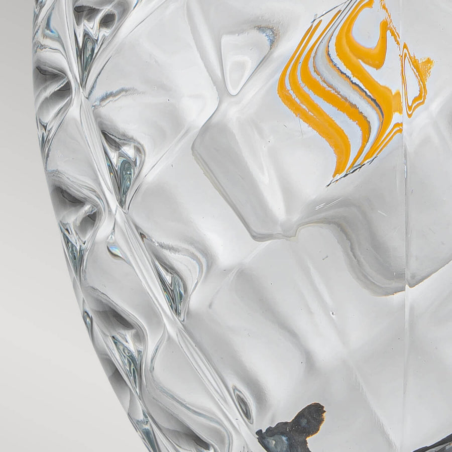 Détail du verre transparent facetté montrant des reflets blancs et une tache orangée