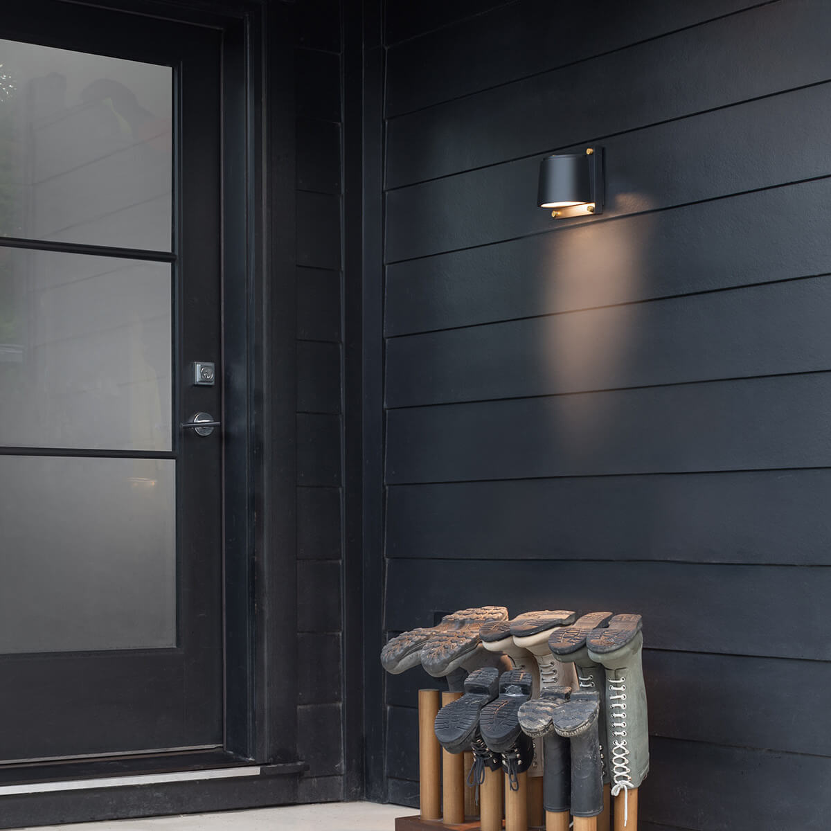 Mise en ambiance de l'applique allumée sur une façade noire avec bottes