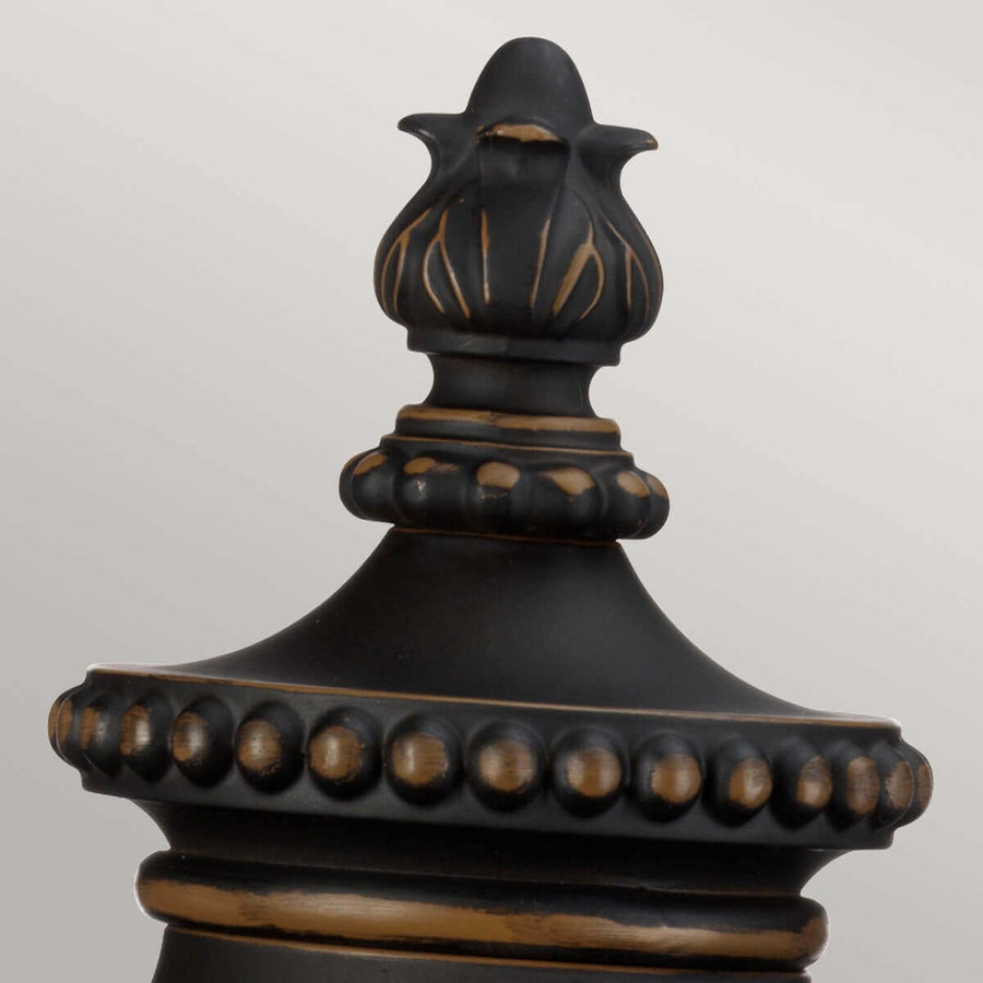 Détail du sommet mouluré avec fleuron, bille dorée et finition bronze vieilli.