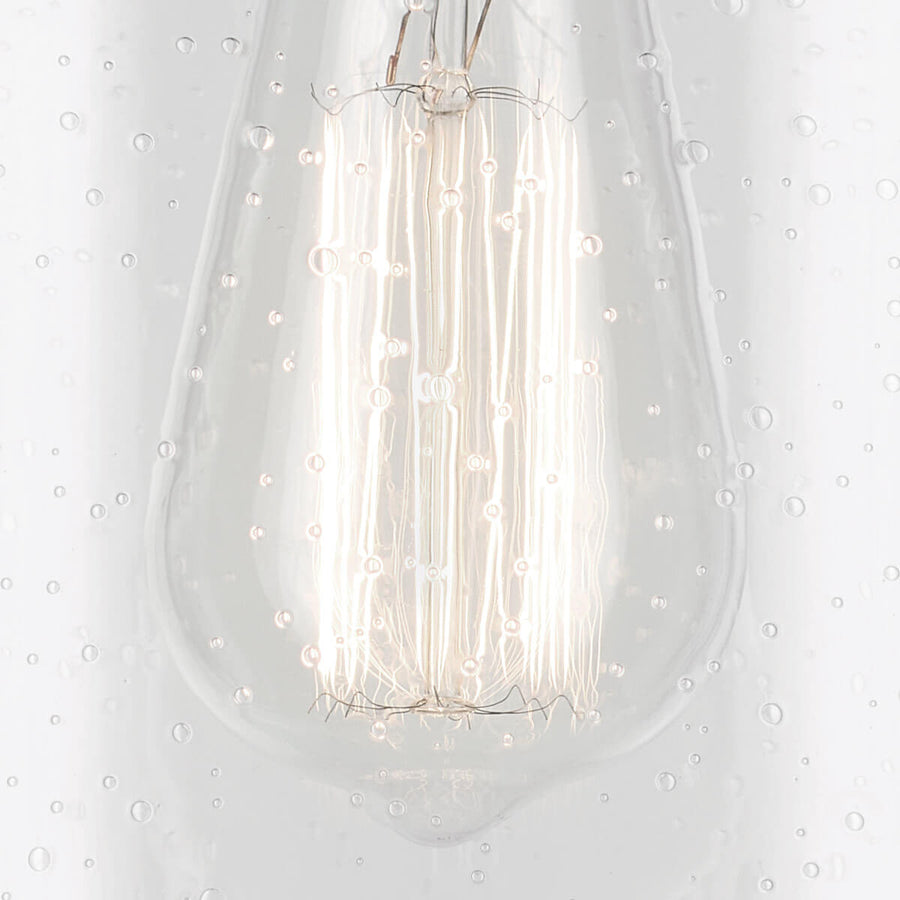 Détail de l’ampoule à filament allumée derrière le verre bullé.