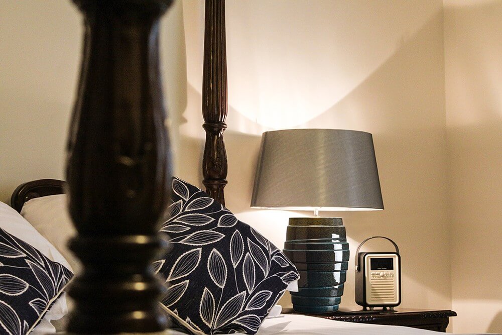 Mise en ambiance dans une chambre, lampe allumée posée sur une table de nuit en bois