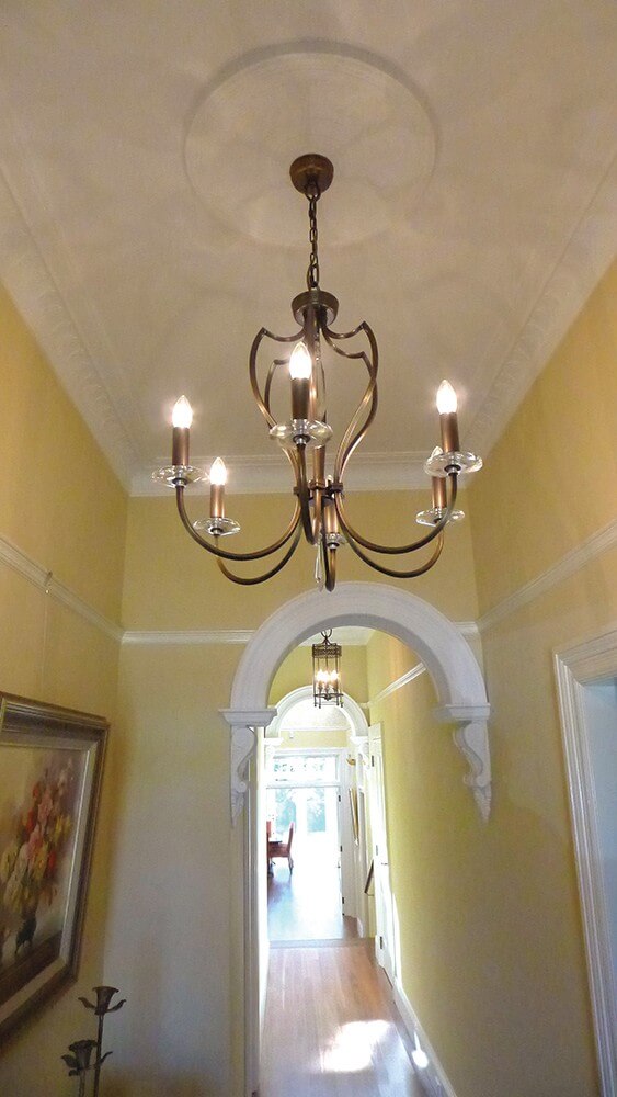 Lustre suspendu dans un couloir jaune avec arche blanche et rosace de plafond