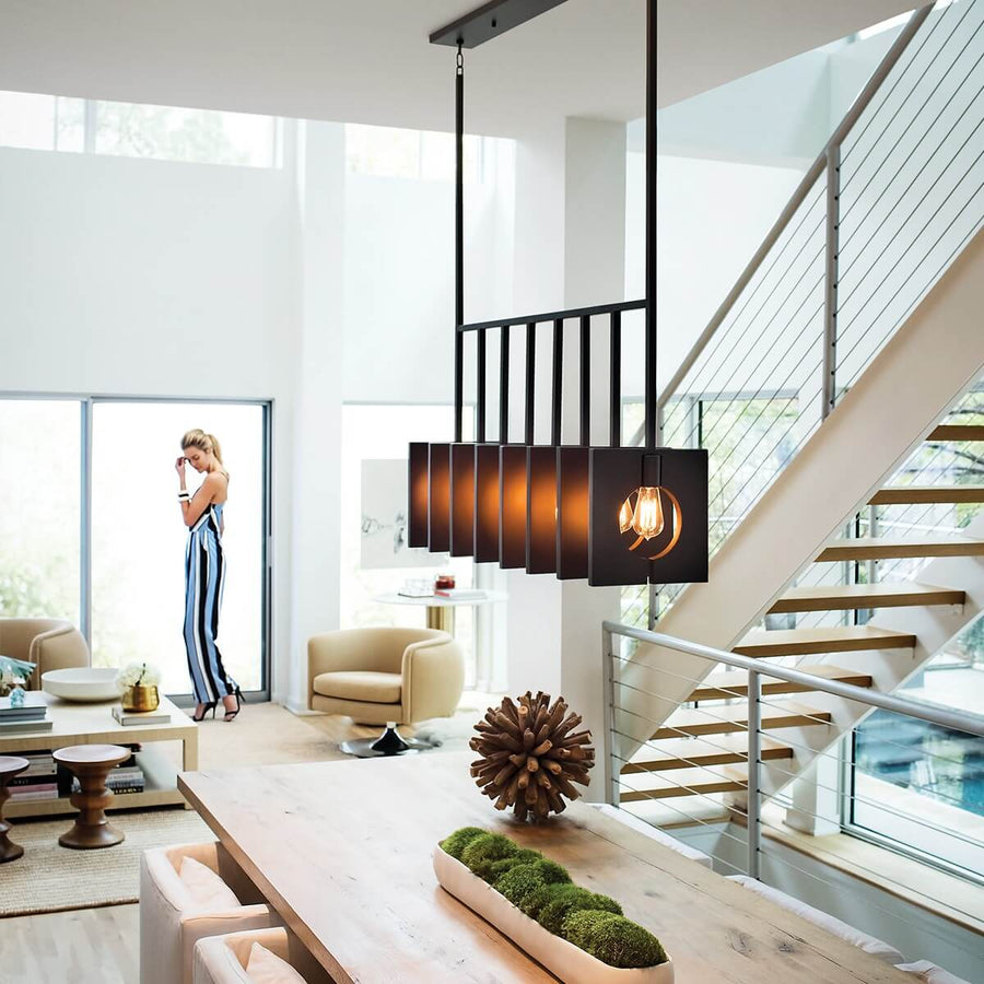 Suspension anthracite installée au-dessus d'une table dans un séjour moderne avec escalier et grande baie vitrée.