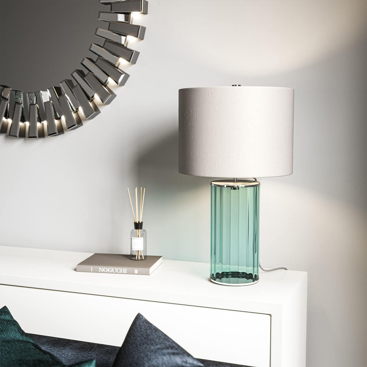 Mise en ambiance de la lampe allumée sur un meuble blanc, avec miroir et parfum d'intérieur.