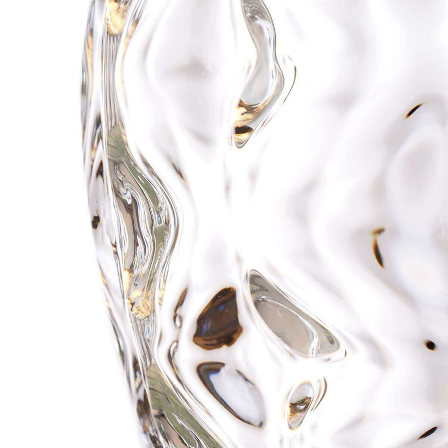 Gros plan sur la texture martelée du verre et ses reflets dorés.