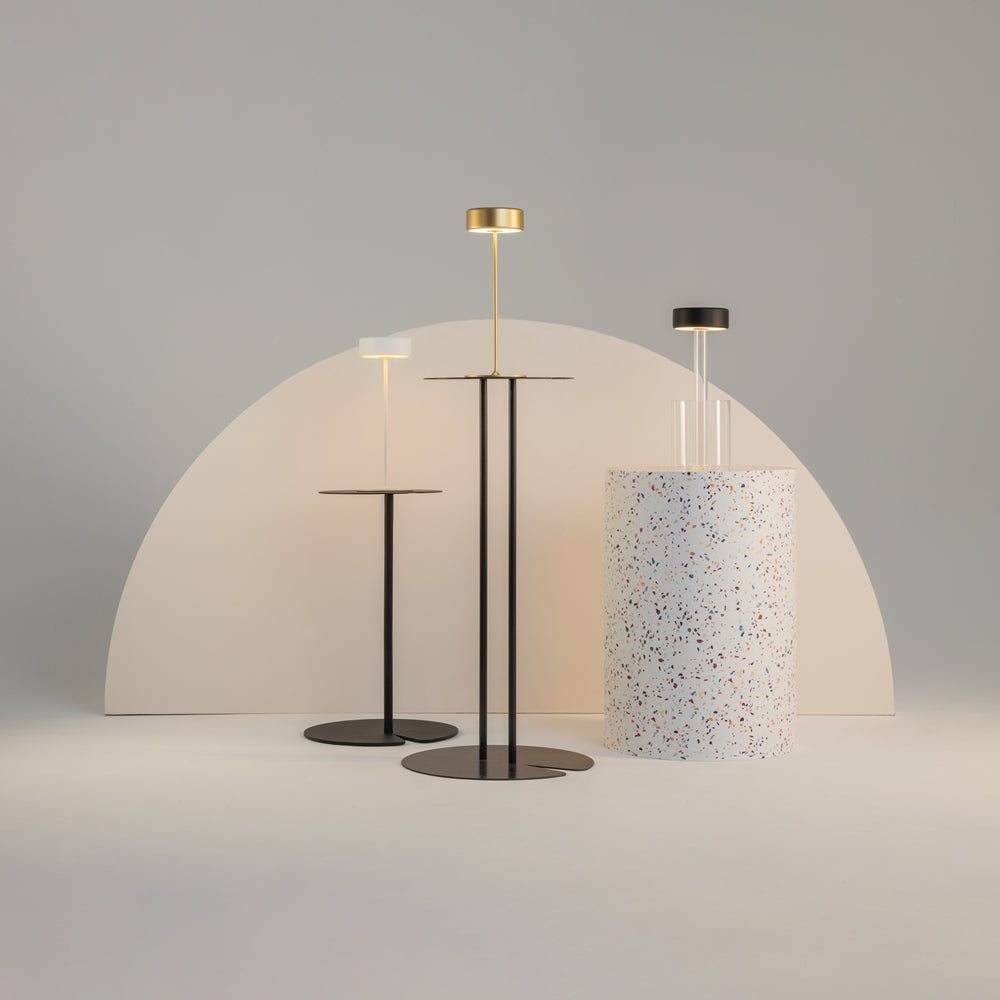 Trois luminaires design exposés devant une arche beige, dont la lampe en verre transparent.