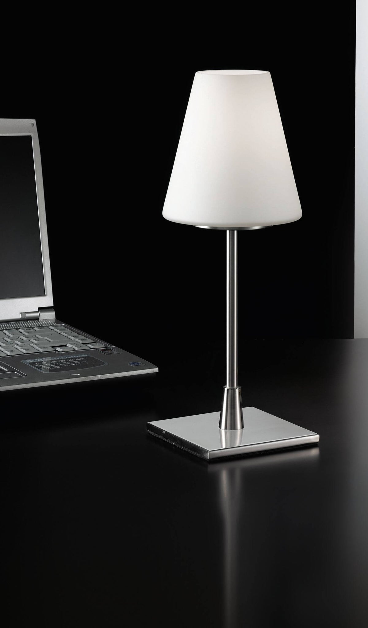 Lampe allumée posée sur bureau noir, près d'un ordinateur portable, ambiance de travail