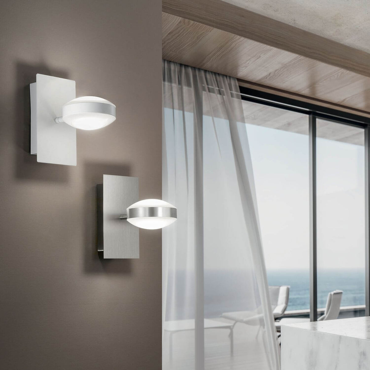 Deux appliques murales allumées dans un intérieur contemporain, l'une blanche, l'autre chromée, vue sur la mer
