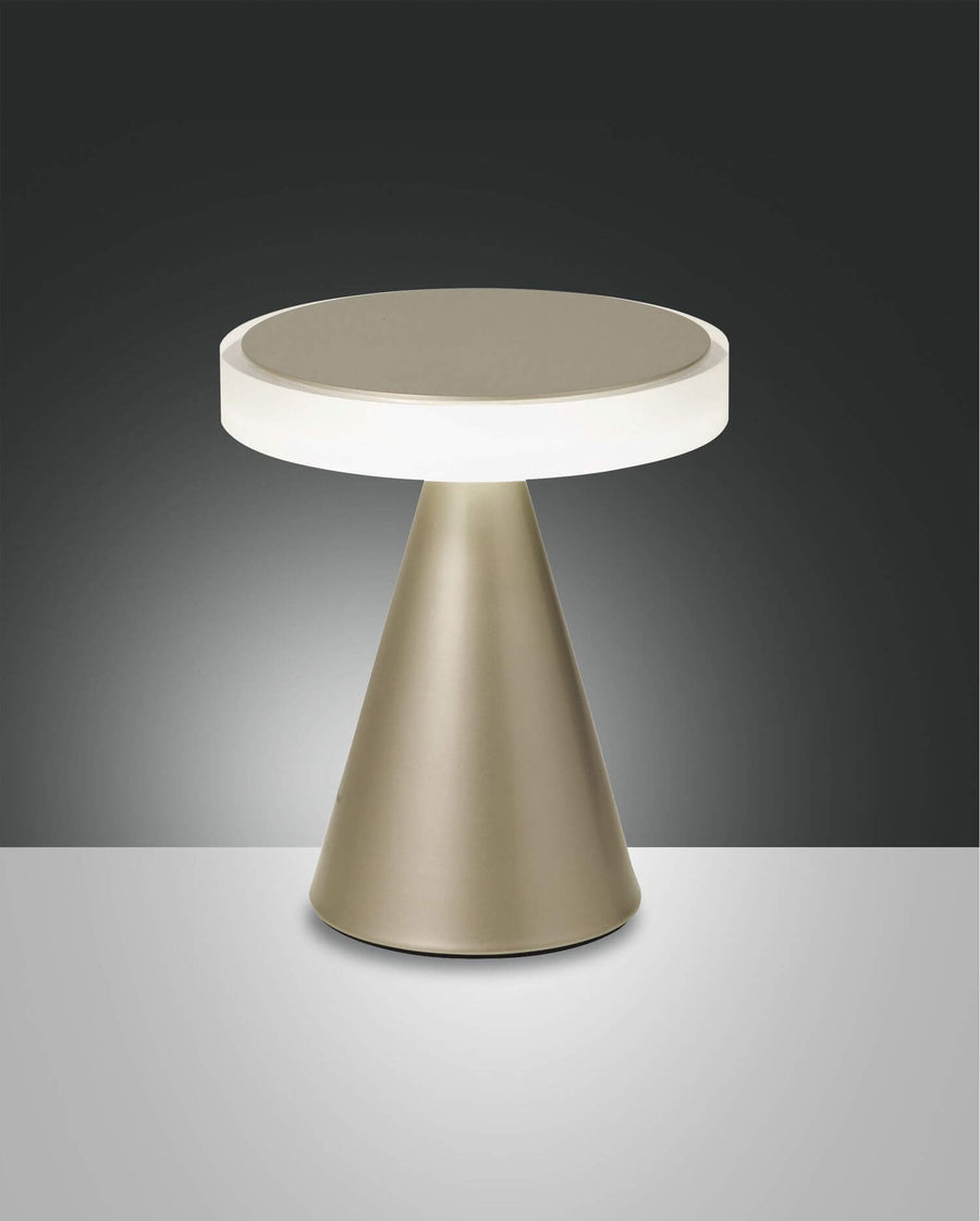 Lampe à poser dorée de face sur fond dégradé, base conique et disque lumineux.
