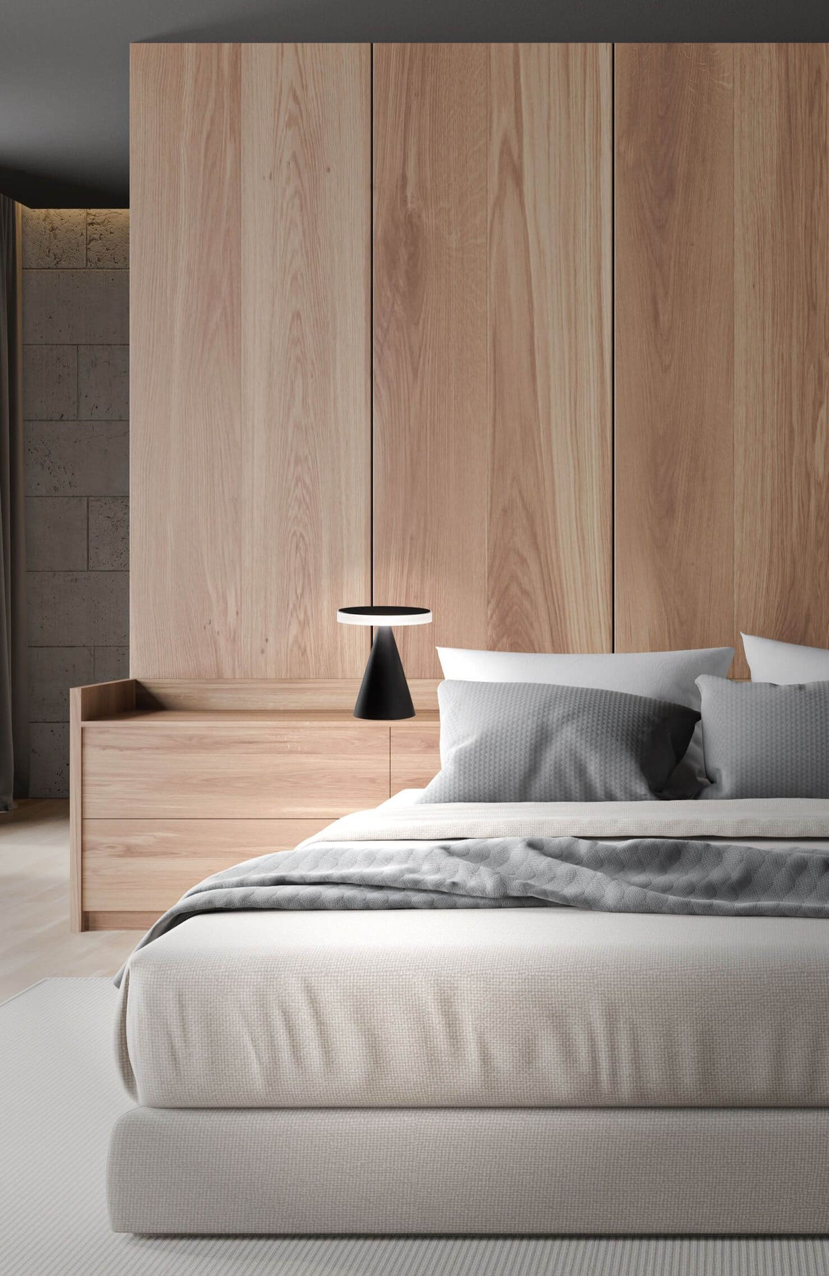 Chevet en bois avec la lampe noire allumée, chambre et lit en arrière-plan.
