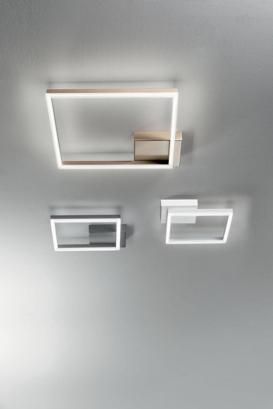 Trois déclinaisons du luminaire fixées au plafond, finitions blanc, gris et doré