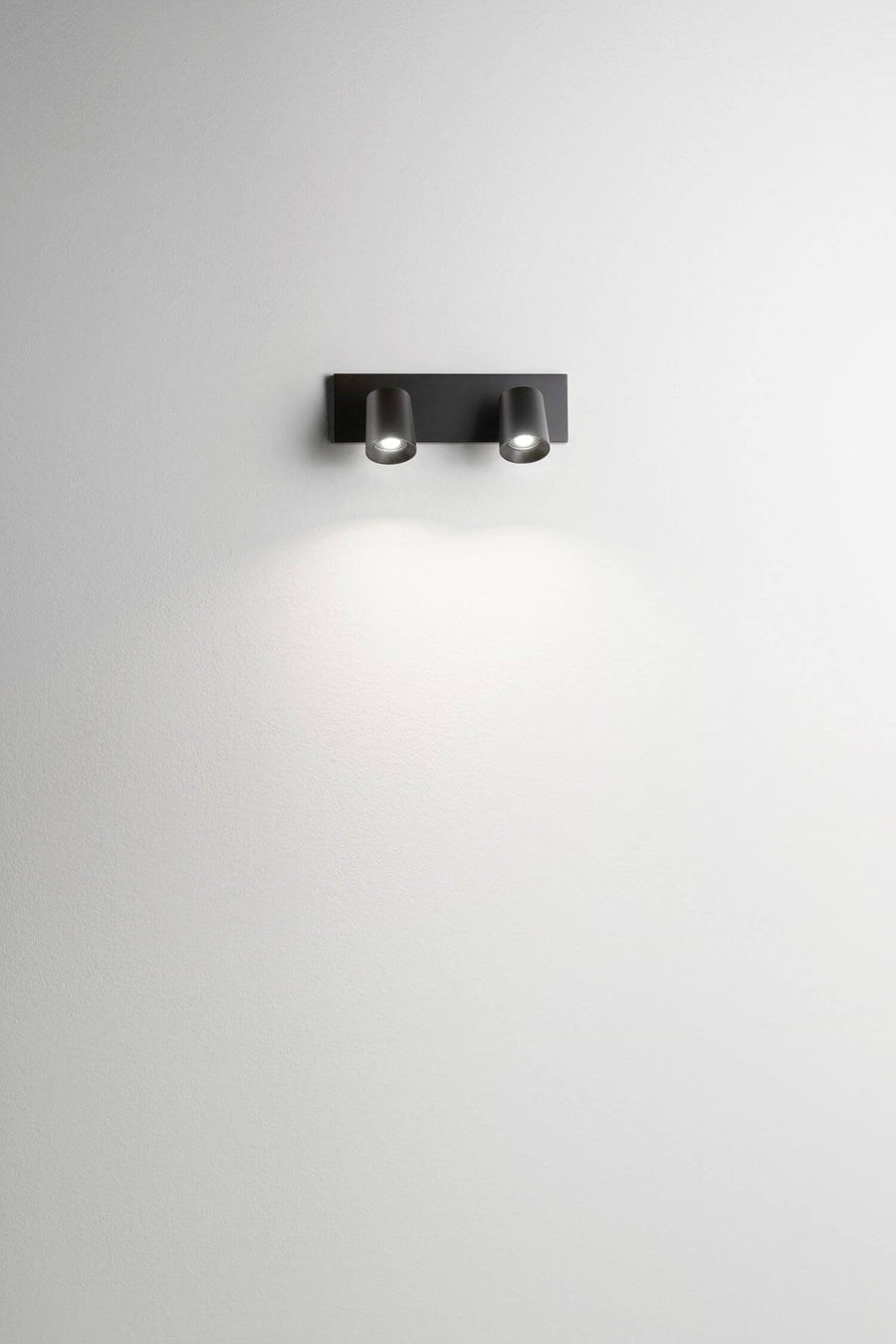 Spot mural deux lumières noir sur mur blanc, halo lumineux diffus