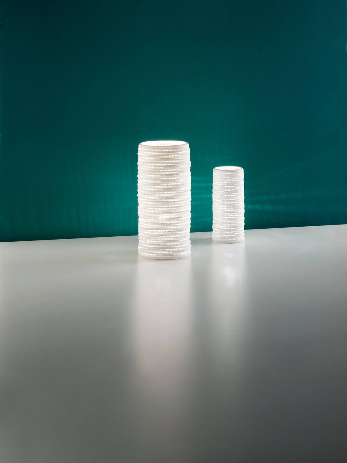 Deux lampes cylindriques blanches de tailles différentes sur fond turquoise