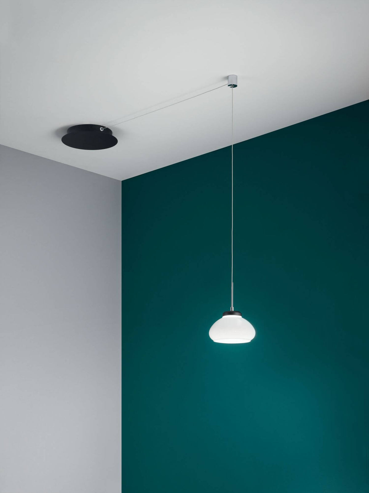 Mise en ambiance du luminaire éclairé devant un mur vert canard et gris