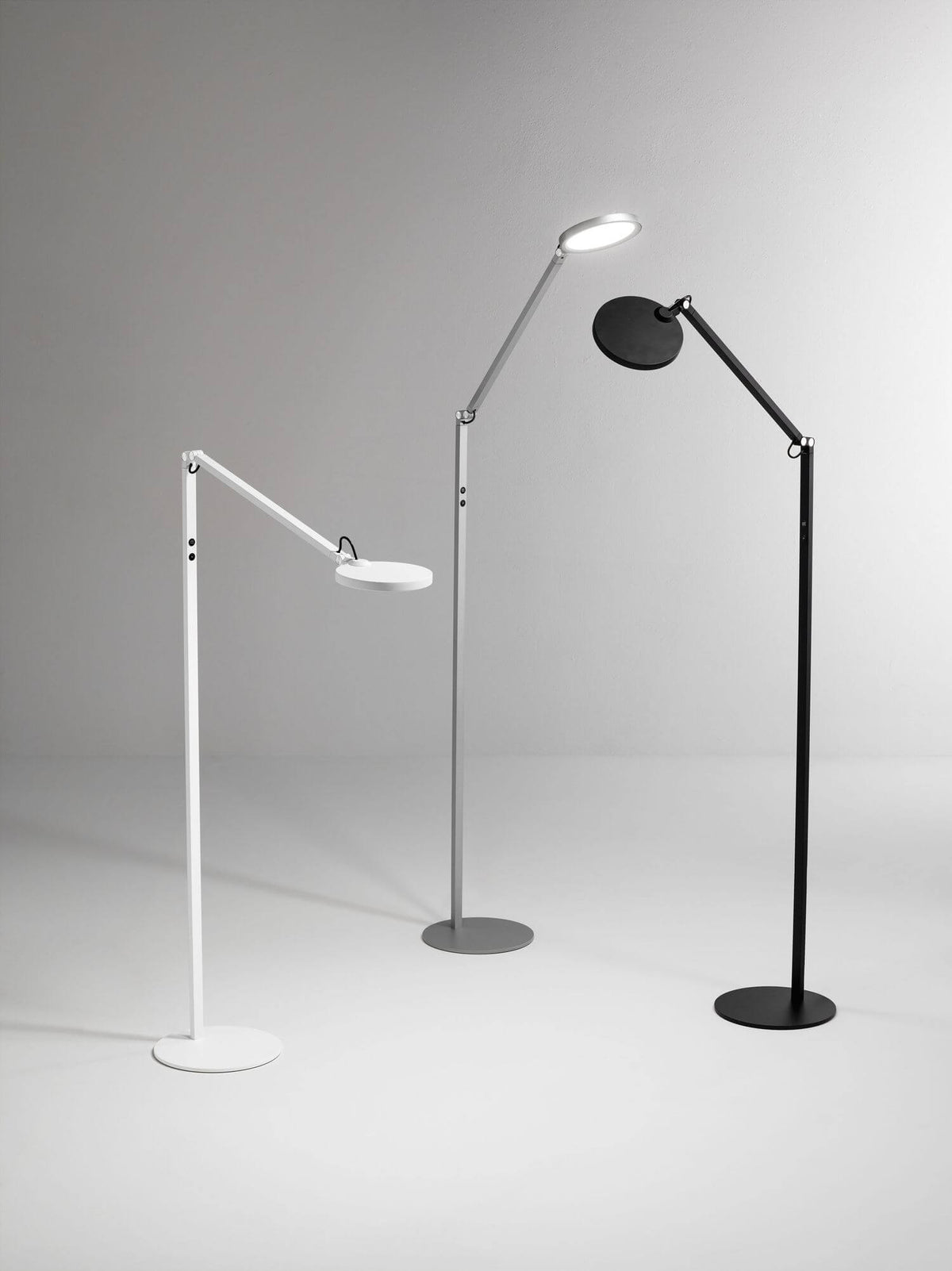 Trois lampes sur pied identiques en blanc, gris et noir, présentées côte à côte