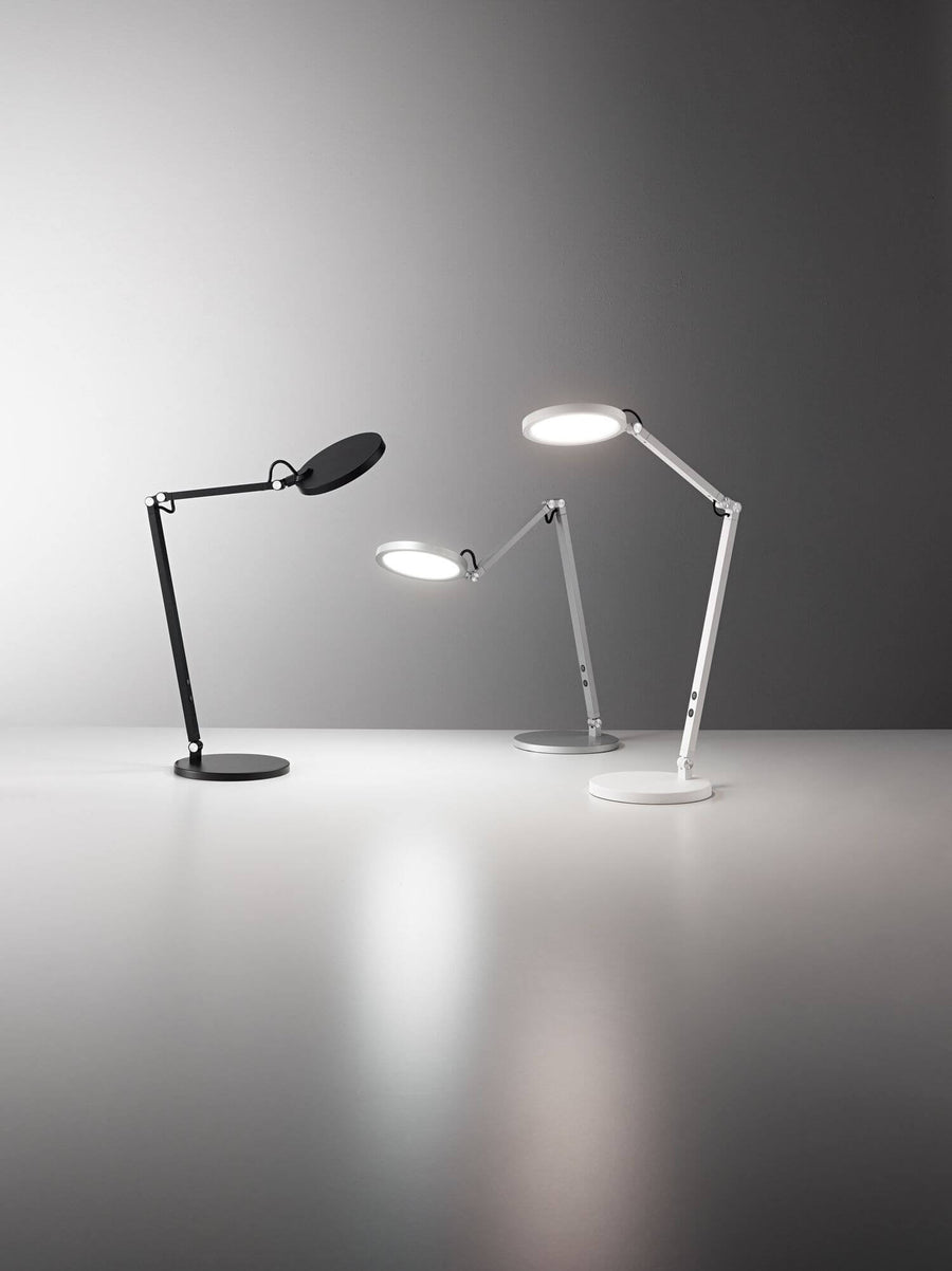 Trois lampes à poser articulées, noire, blanche et argentée, présentées côte à côte.
