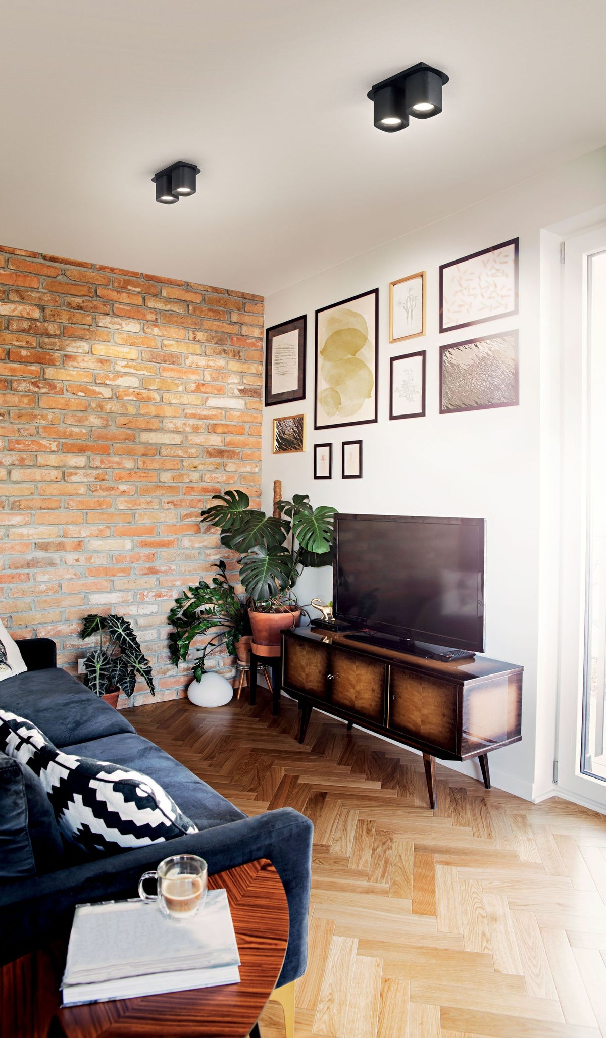 Mise en ambiance dans un salon avec briques, deux spots doubles noirs au plafond.