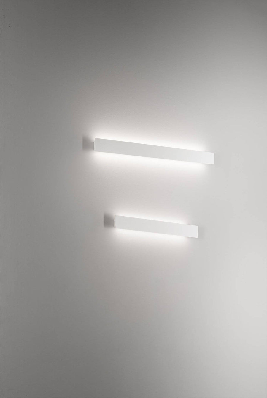 Deux appliques murales allumées sur mur blanc, vue plongeante et décentrée