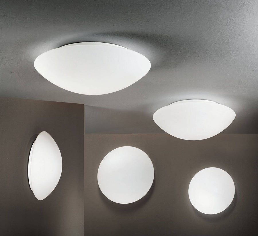 Plusieurs luminaires blancs ronds ou ovales, fixés au plafond et au mur, dans un intérieur gris.