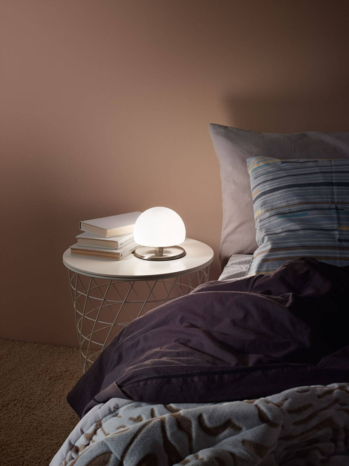 Mise en ambiance nocturne, lampe allumée sur table de chevet près d'un lit.