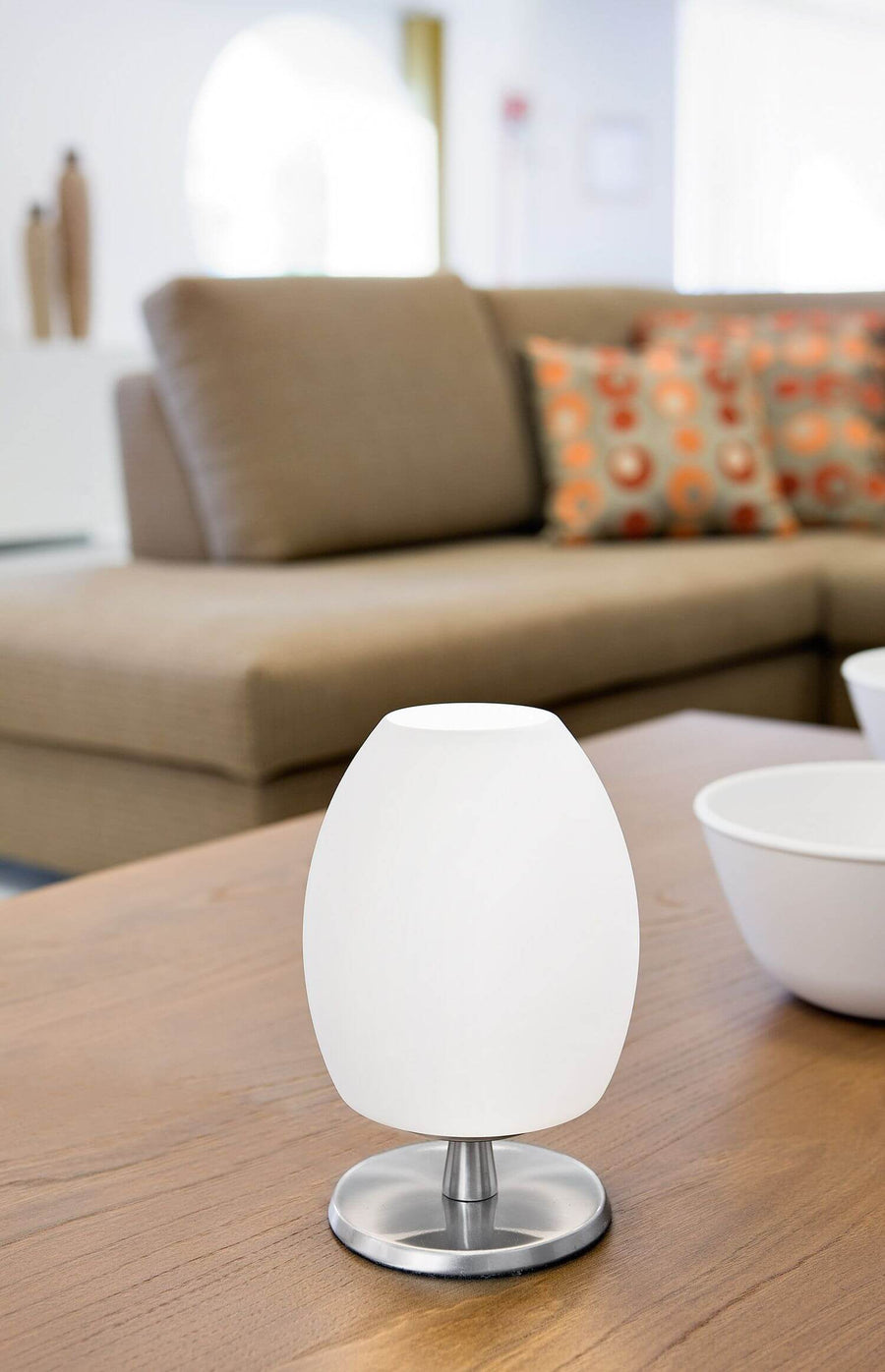 Lampe blanche posée sur table en bois devant canapé beige flou.