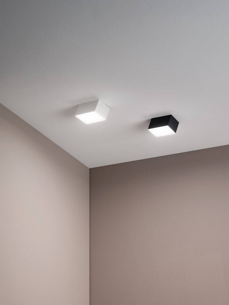 Deux plafonniers carrés, un blanc et un anthracite, au plafond d'un angle