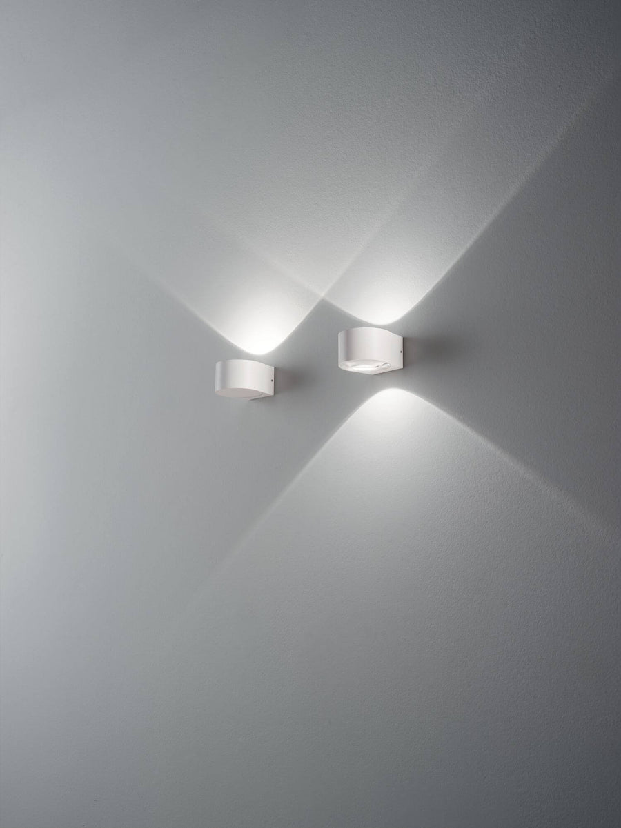 Deux appliques blanches allumées projetant des faisceaux lumineux croisés sur un mur
