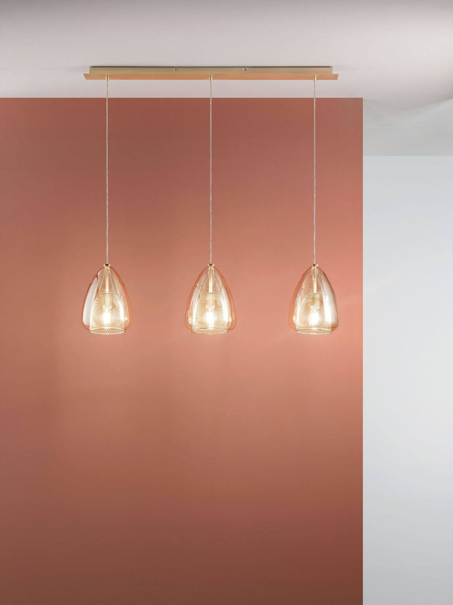 Vue en situation, trois suspensions ambrées allumées devant un mur terracotta.