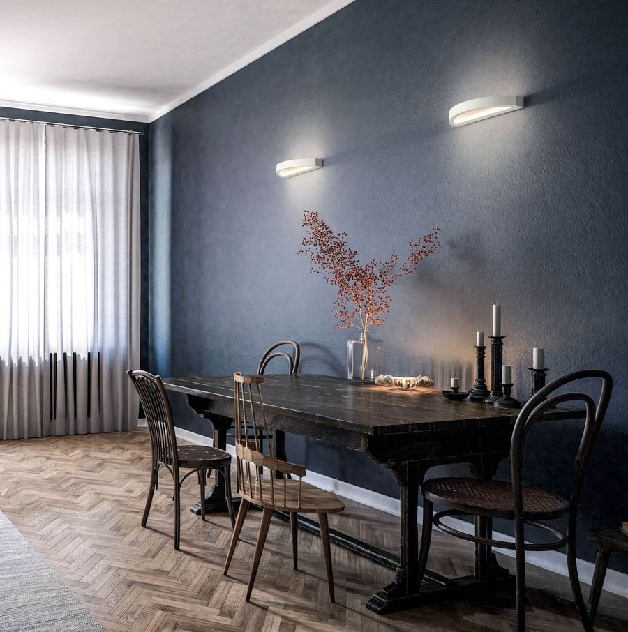 Deux appliques murales fixées sur un mur bleu foncé au-dessus d'une table à manger.
