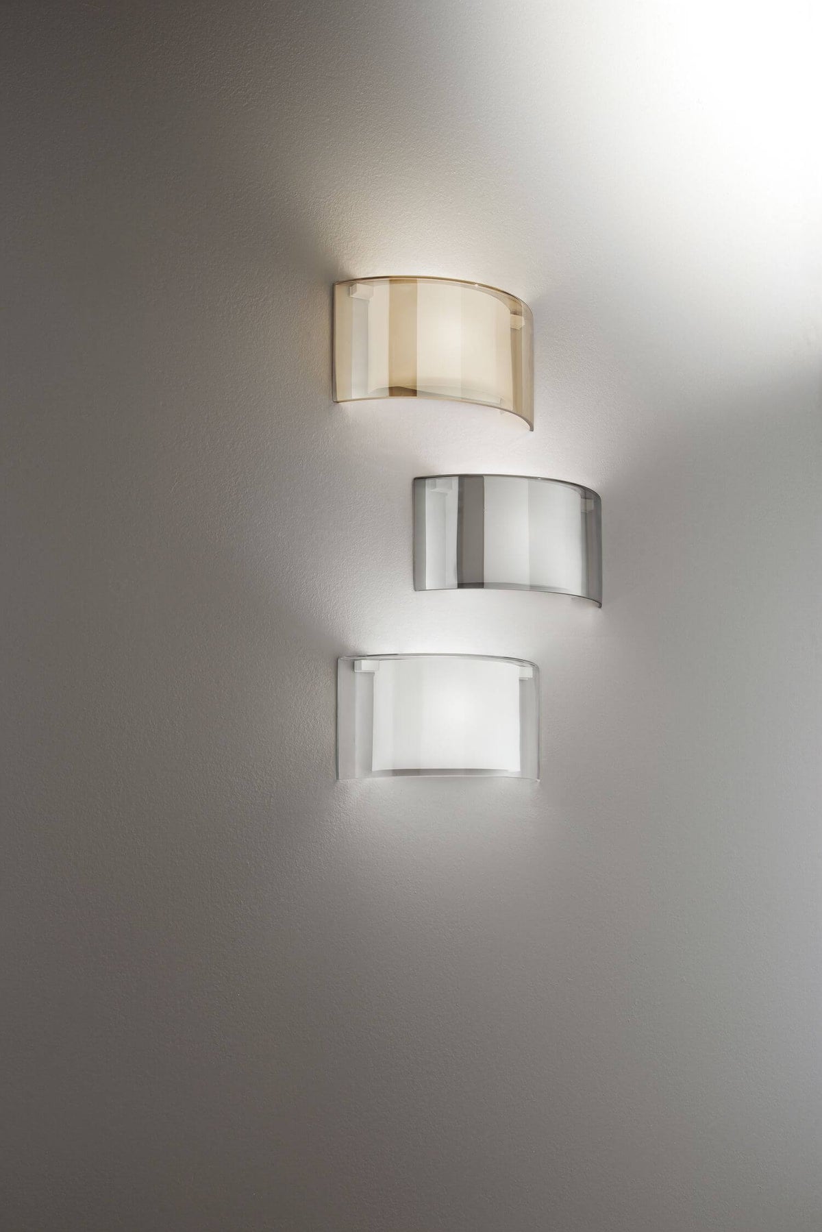 Trois appliques murales alignées verticalement : verre ambré, fumé gris et blanc translucide