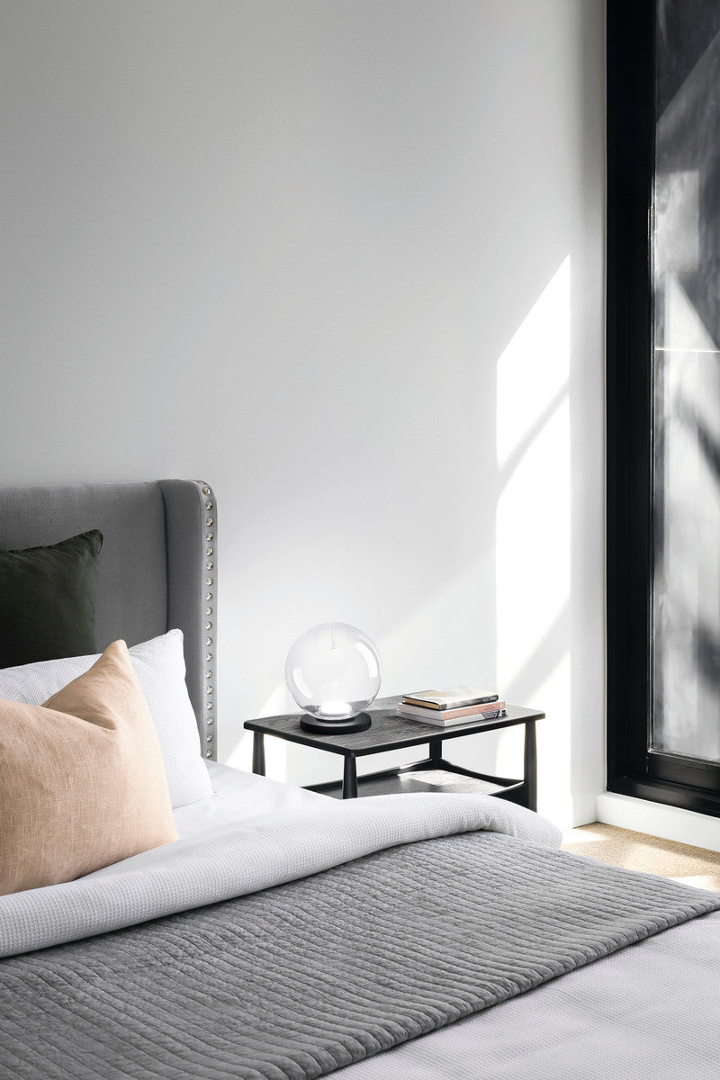 Lampe sphérique transparente posée sur une table de chevet en bois, près d'un lit