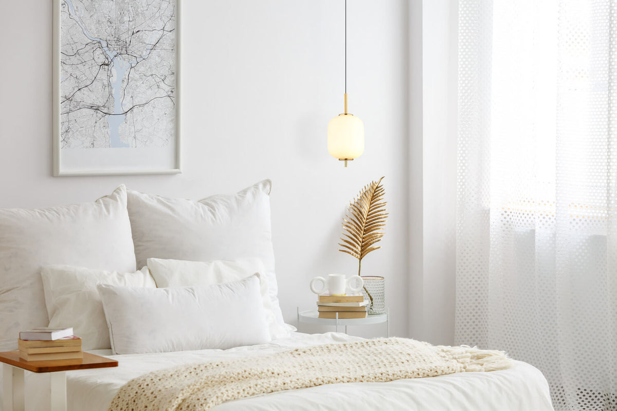 Mise en ambiance : suspension dorée allumée près d'un lit aux coussins blancs