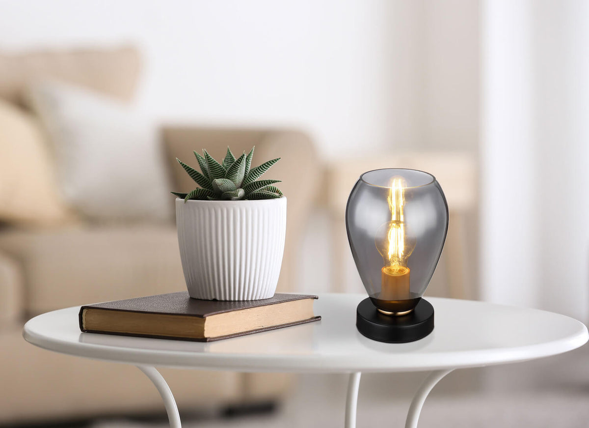 Mise en ambiance de la lampe noire sur une table basse blanche avec livre et plante.