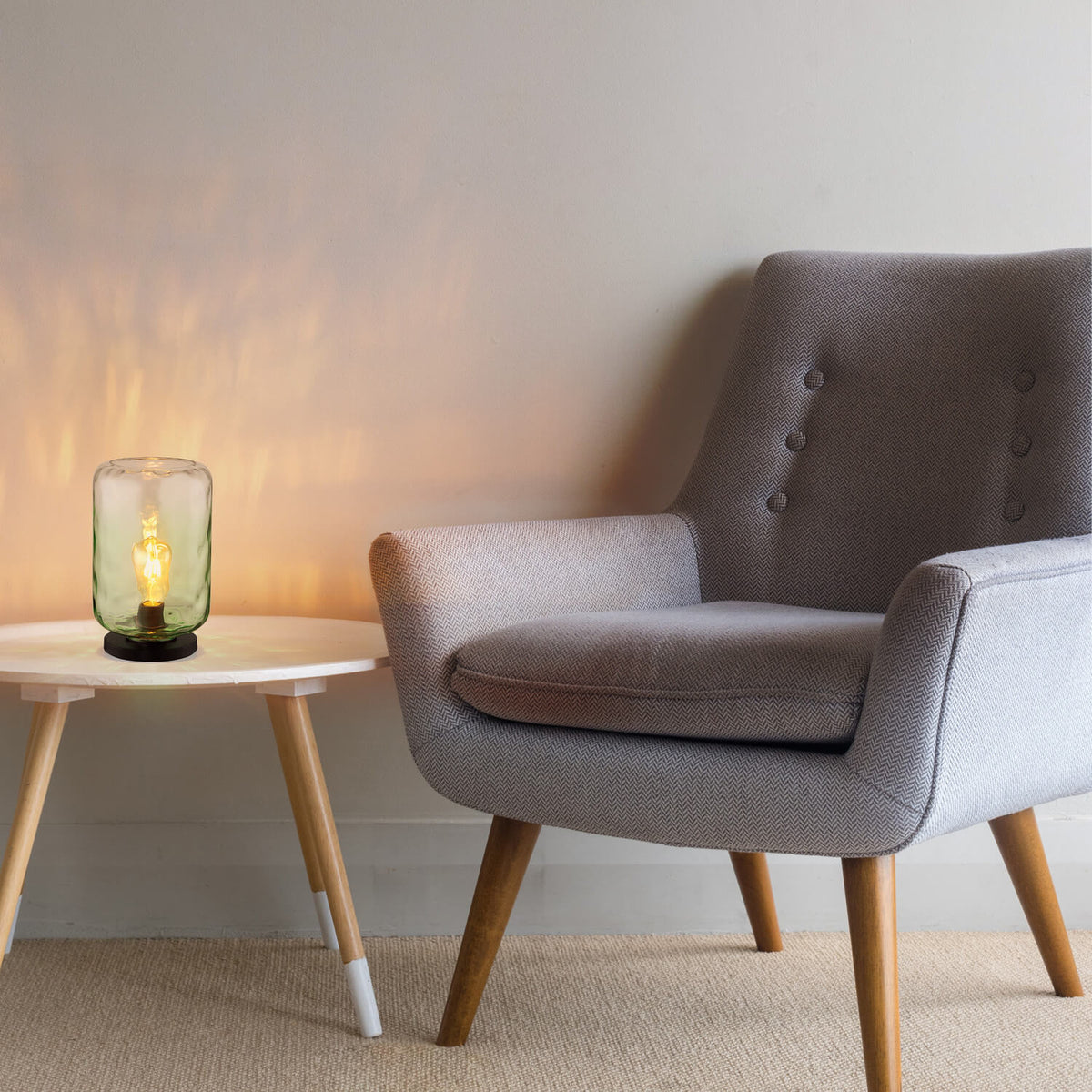 Lampe posée sur une table basse, près d’un fauteuil gris, éclairant le mur