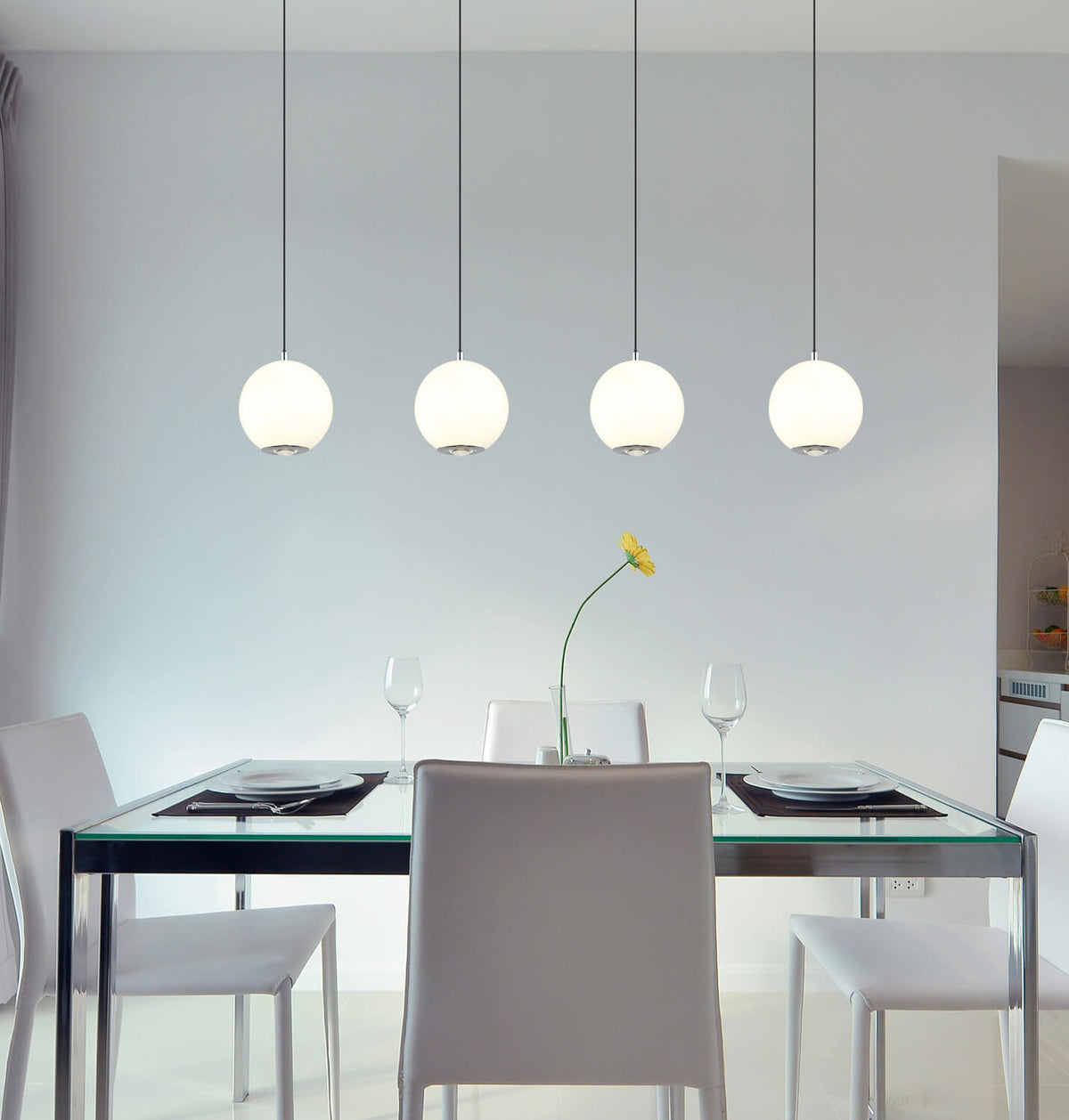 Mise en ambiance salle à manger avec suspension quatre globes blancs allumés au-dessus table verre.
