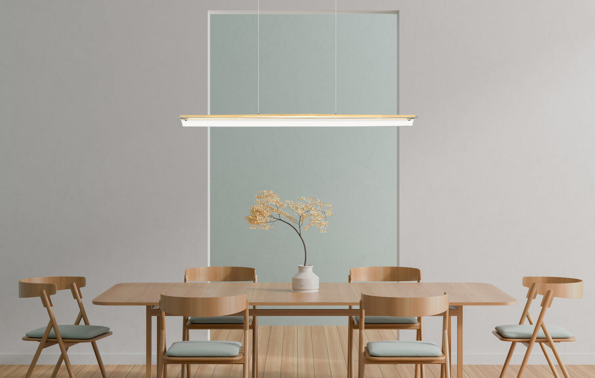 Suspension linéaire dorée installée au-dessus d'une table à manger en bois, ambiance minimaliste.