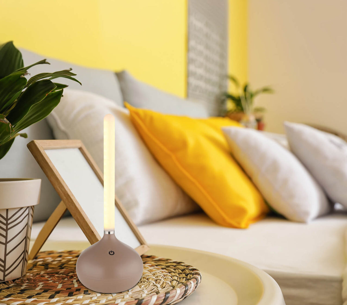Mise en ambiance sur table basse en rotin, canapé jaune et coussins clairs.